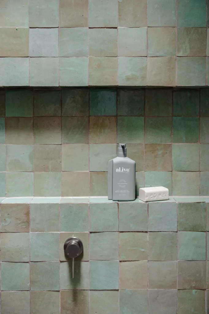 A close up shot of a shower in an ensuite bathroom with green zellige wall tiles, a shower niche clad in the same tiles and tapware in brushed nickel.