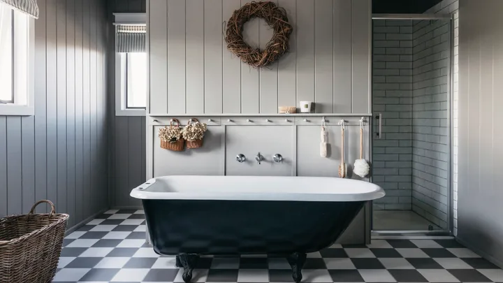Elegant bathroom with a black clawfoot tub, gray walls, checkered floor, woven wreath, and glass shower.