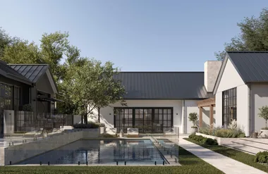 Modern house with large windows, metal roof, garden, and a fenced swimming pool under a clear blue sky.